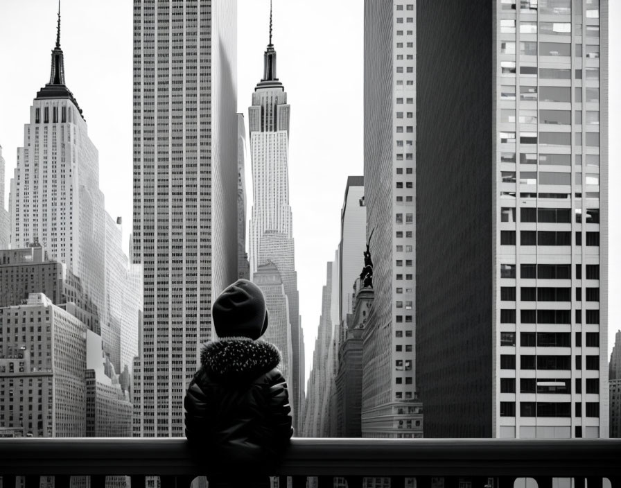 Person in winter jacket gazes at grayscale cityscape with skyscrapers from high viewpoint