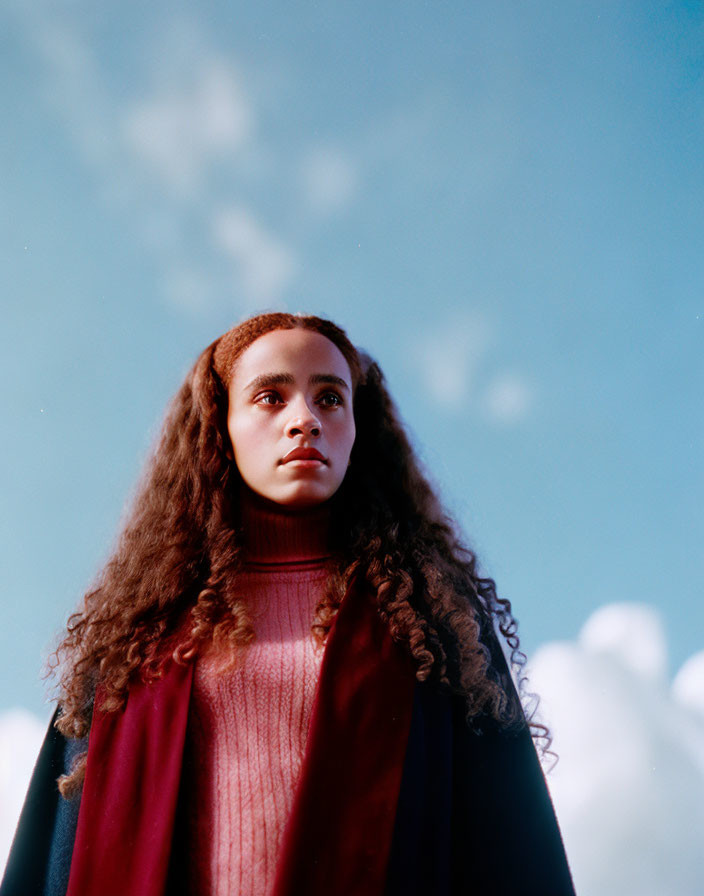 Curly-Haired Person in Red Turtleneck and Coat Against Blue Sky