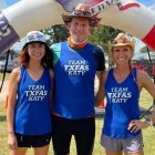 Three athletes in racing-themed attire posing confidently near a jet engine smoke trail.