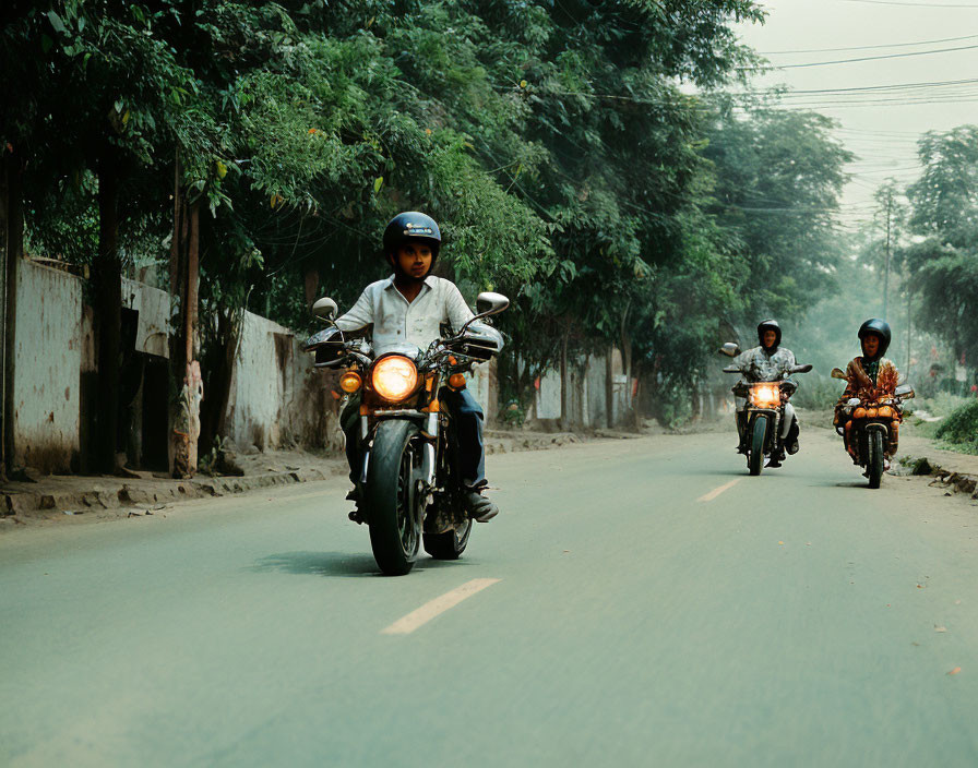 Three motorcyclists on tree-lined street, lead rider in focus