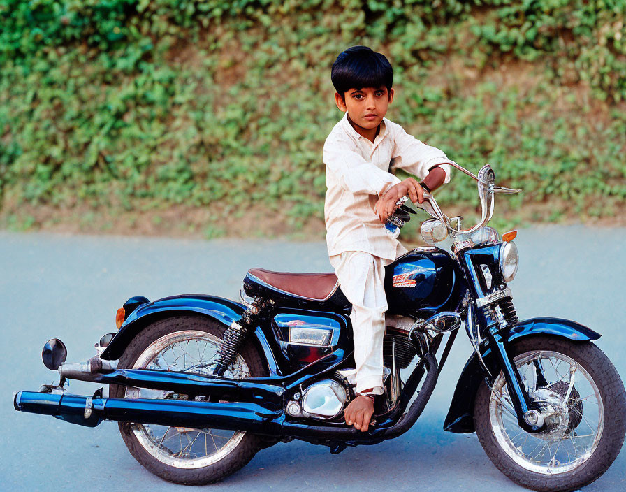 Young boy in traditional attire on black motorcycle gazes at camera