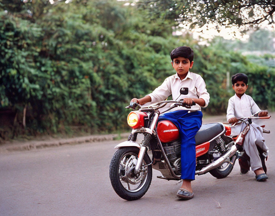 Two young boys in school uniforms riding toy motorcycles on tree-lined road