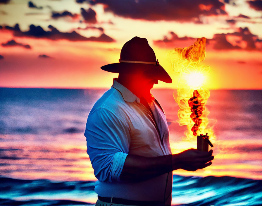 Silhouette of person with hat holding flaming object by ocean at sunset