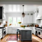 Contemporary kitchen with white cabinets, stainless steel appliances, central island, chandelier, and scenic green