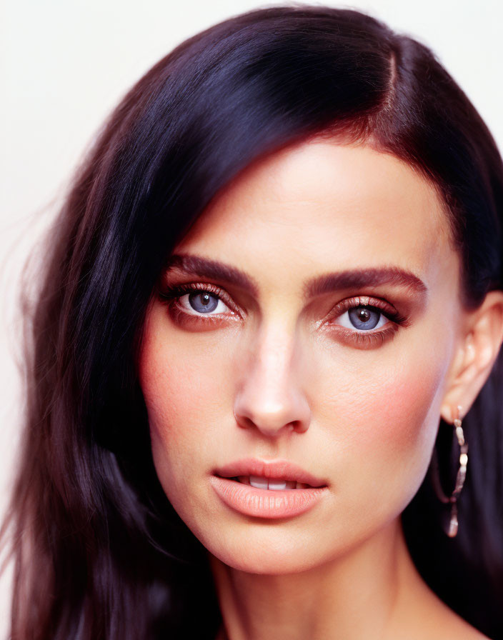 Portrait of woman with dark hair and intense gaze against soft backdrop