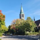 Vibrant autumn landscape with steepled building and people walking.