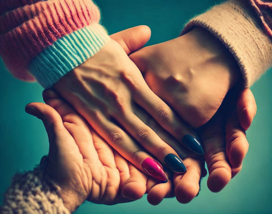 Colorful fingernails cradled in two hands on teal backdrop