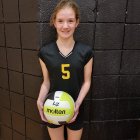 Female volleyball player in dark uniform ready to play in gym with net.