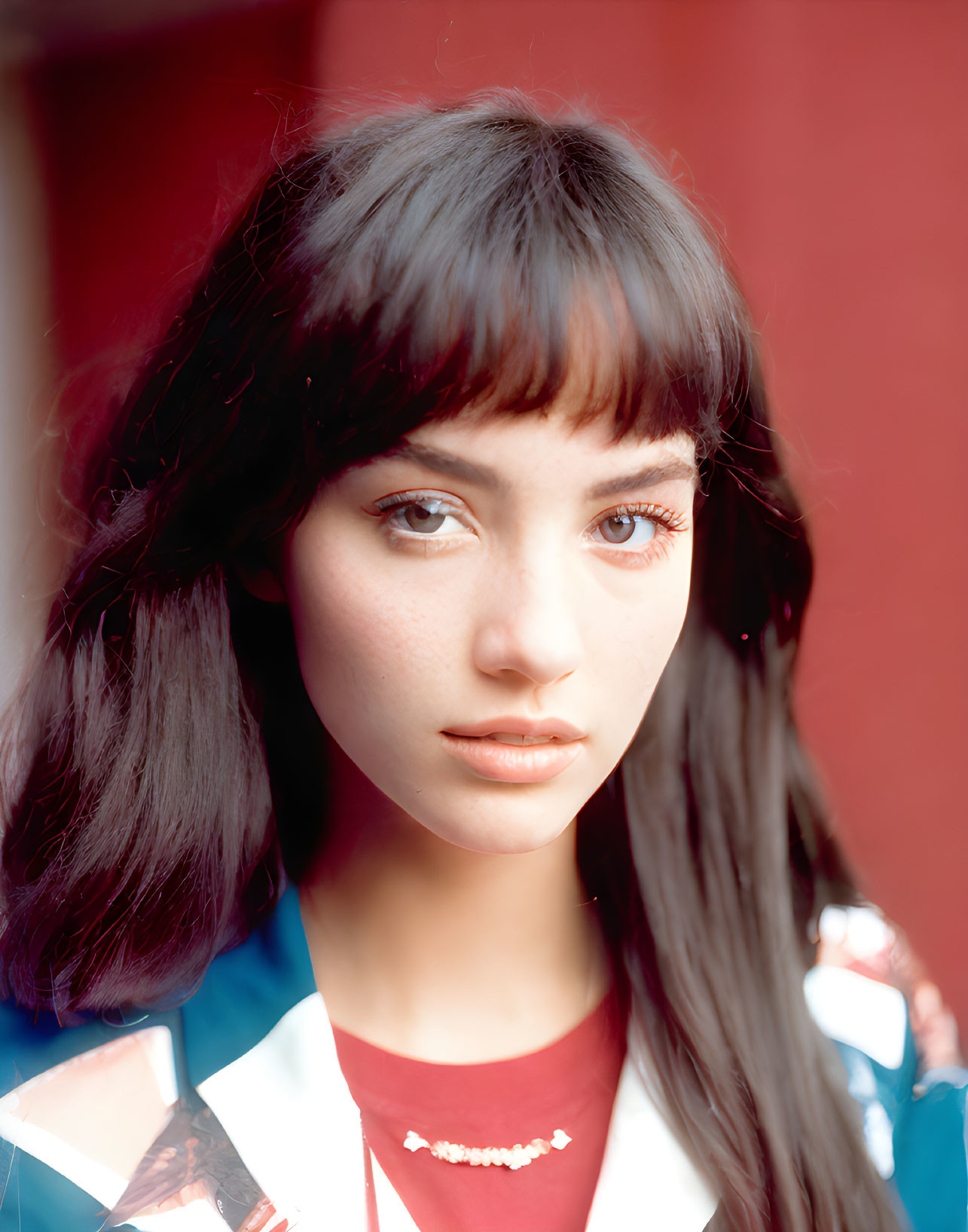 Portrait of a young woman with dark hair and blue eyes in red and white attire on a red backdrop