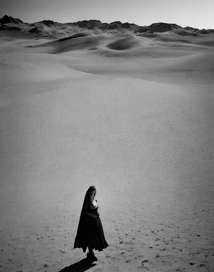 Lonely figure in dark clothes among vast sand dunes under clear sky