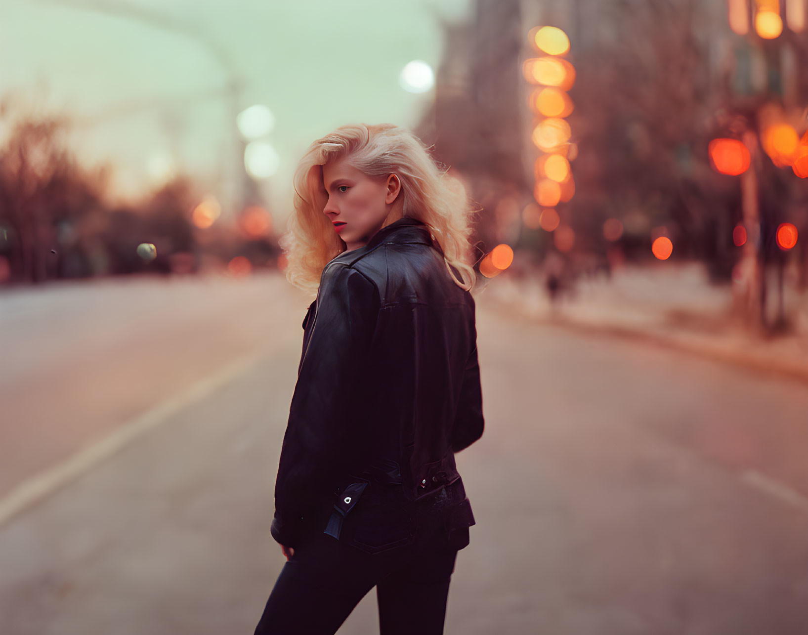 Woman in Black Leather Jacket Stands in City Street at Dusk