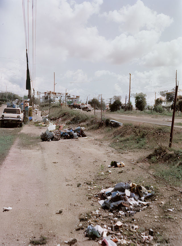 Garbage-filled roadside with cars and cloudy sky