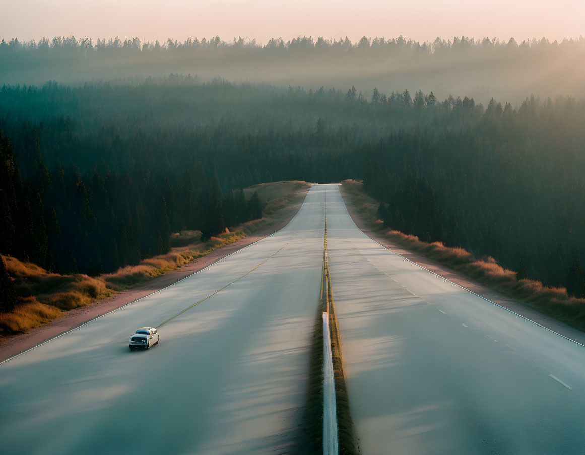 Car driving on misty forest highway at sunrise