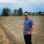 Blue-haired person in galaxy t-shirt poses confidently in rural landscape