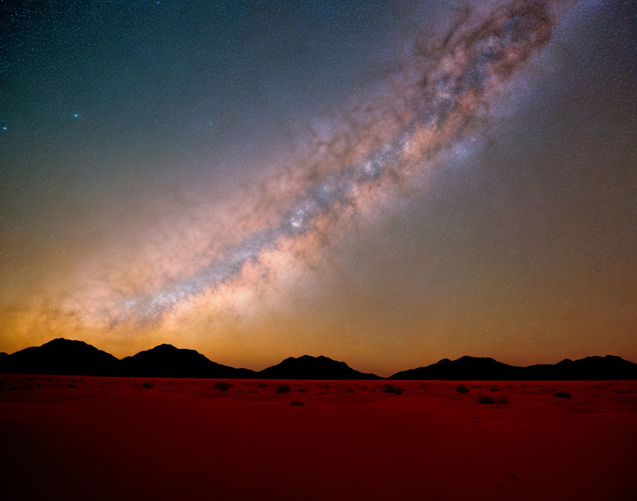 Night sky with Milky Way over mountains and desert terrain.