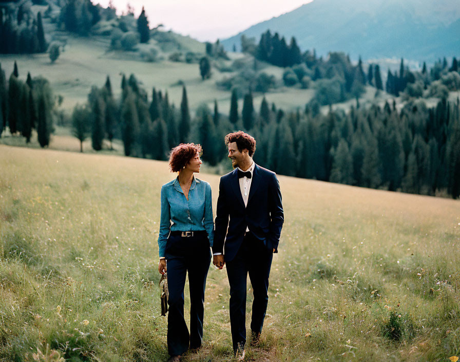 Couple walking hand in hand in lush green meadow with rolling hills.