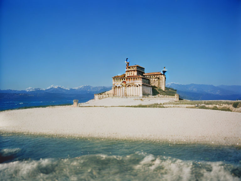 Ancient stone building with columns on sandy beach, blue sky, distant mountains