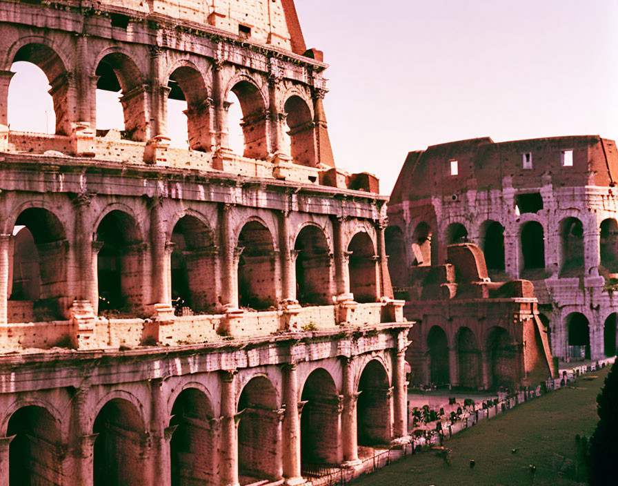 Ancient arches of the Colosseum in Rome with tourists and warm sunlight.