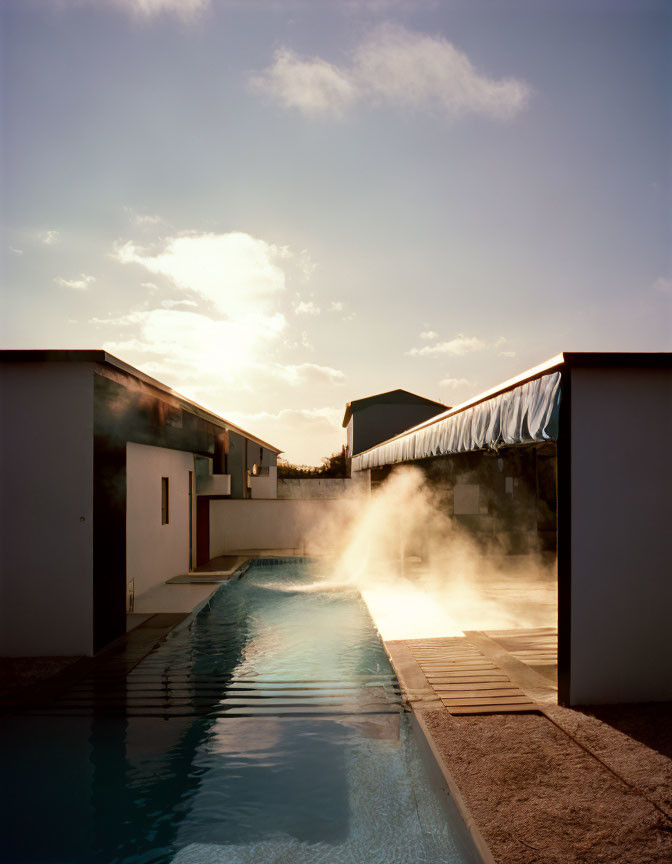 Tranquil poolside scene at dusk with steam, modern buildings, clear sky