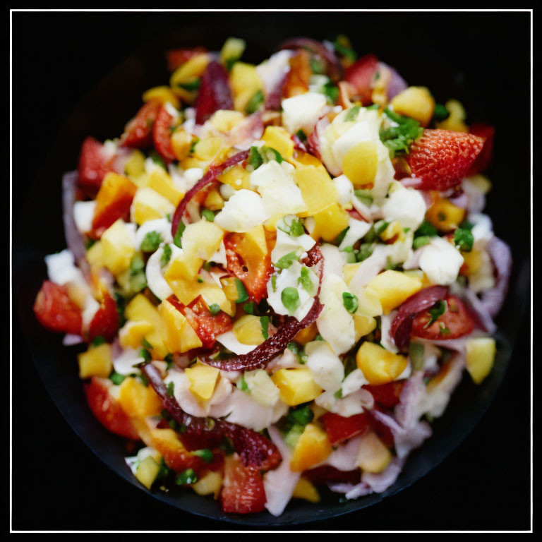 Vibrant fruit salad with strawberries and mango in black bowl