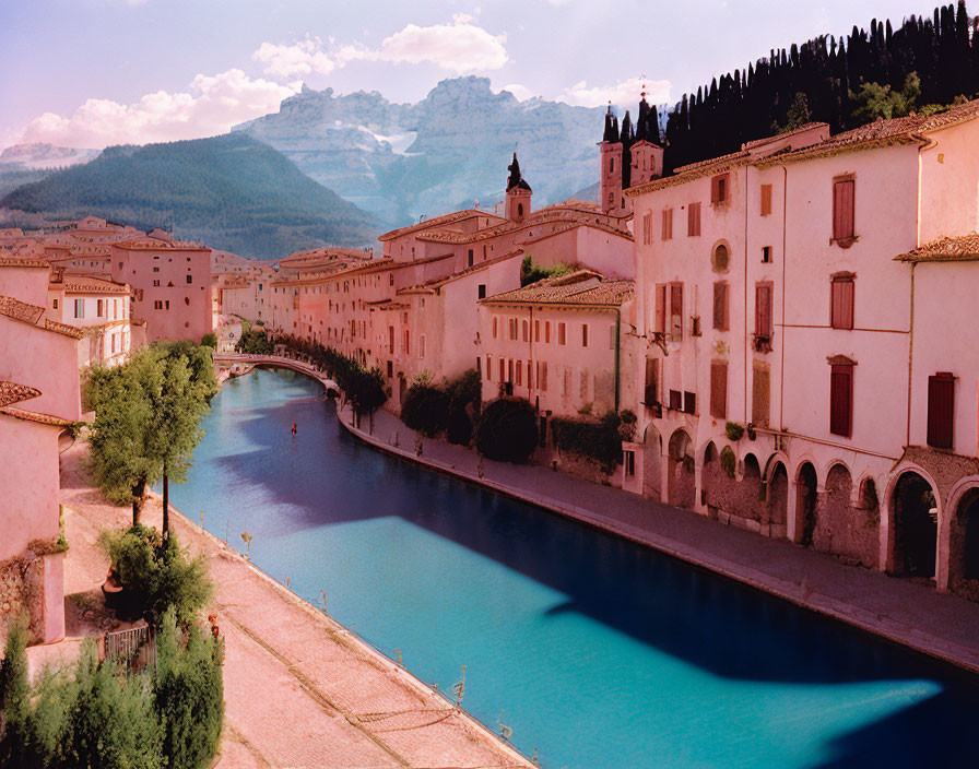 Old European town with historic buildings by calm river, mountains, clear sky