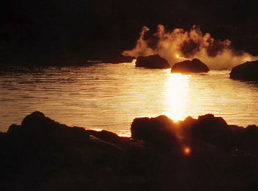 Scenic sunset over rocky shoreline with sun reflection and steam rising