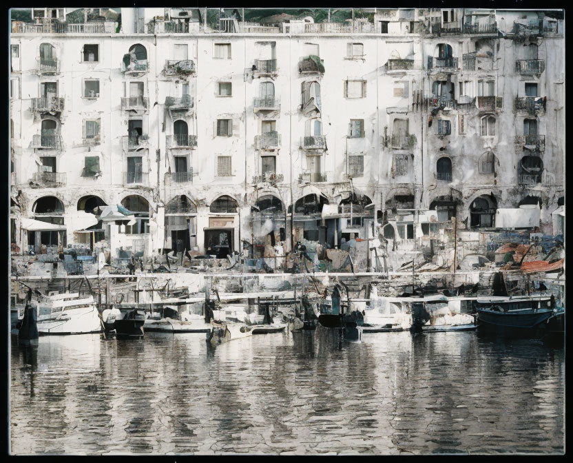 Historic waterfront buildings with multiple arches and boats in a Mediterranean setting.