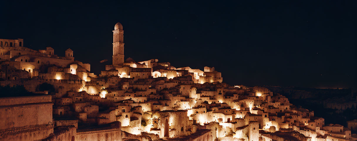 Ancient town night view with illuminated buildings on hill and stone tower under starry sky