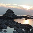 Tranquil sunset scene with rocky outcrop and small structure by calm sea