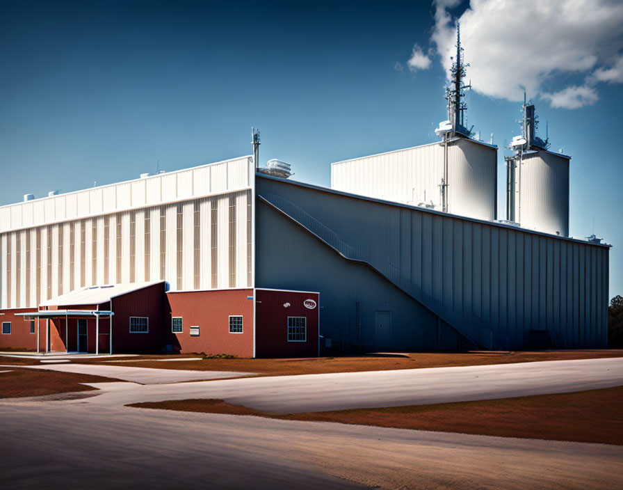 Large white and blue industrial buildings with red accents and antennas under a clear sky.