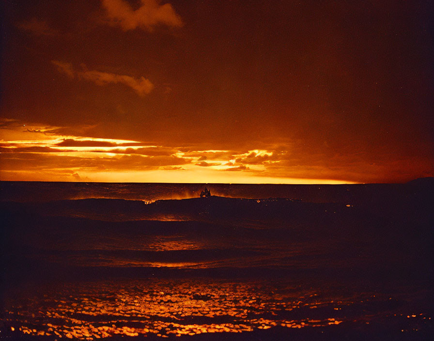 Vibrant sunset over ocean with orange hues and silhouette of person.