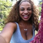 Curly-haired woman in blue off-shoulder top with headband in greenery pose.