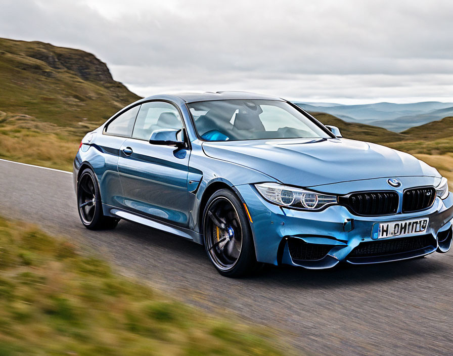 Blue BMW M4 Coupe on Road Amidst Rolling Hills under Cloudy Sky