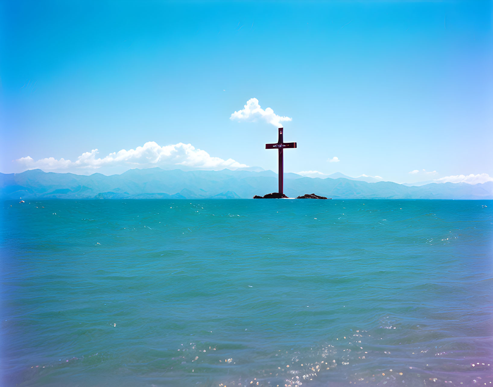 Large Cross on Small Island in Tranquil Sea with Mountains and Clear Sky