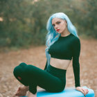 Blue-haired woman on stool in forest with fallen leaves wearing black clothes