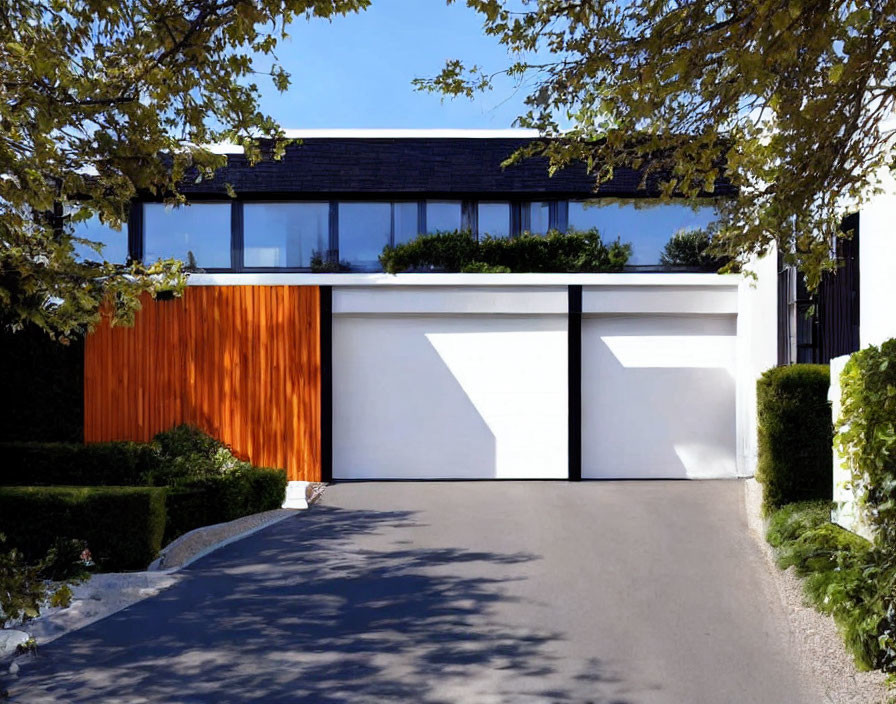 White facade modern house with wooden paneling and large garage door surrounded by green foliage.