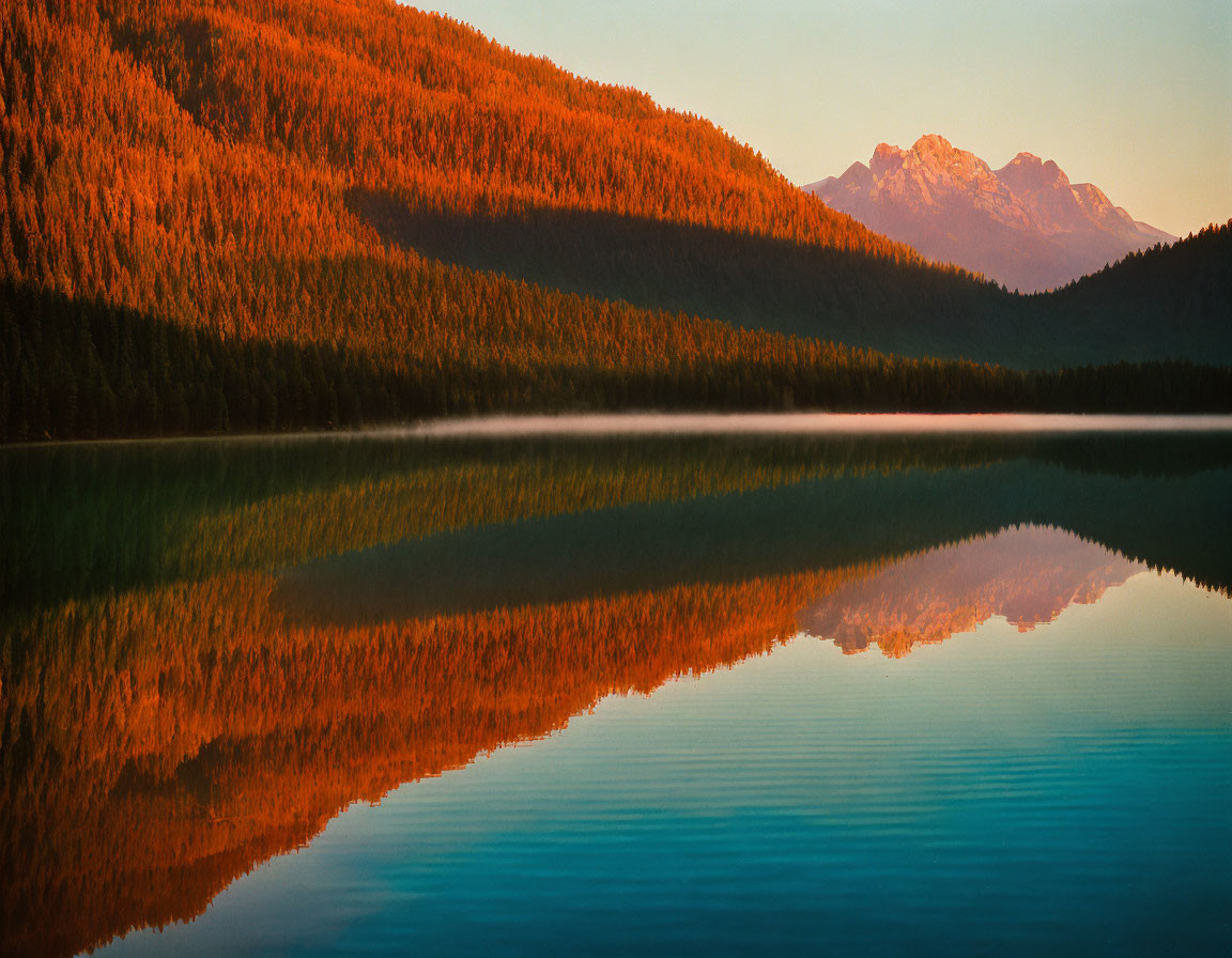 Sunset over forested mountains reflected on serene lake