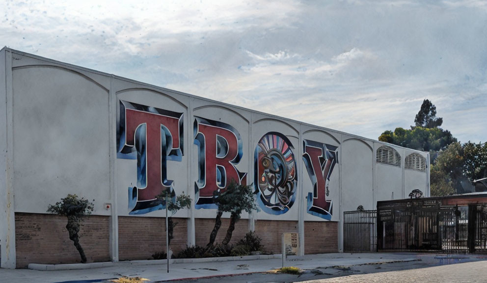 Mural featuring "TROY" word, Trojan helmet, gates, trees under cloudy sky