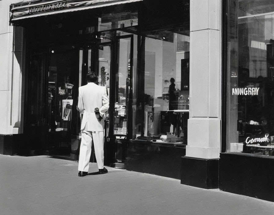 Person in white suit gazes into store on sunny day with shadows.