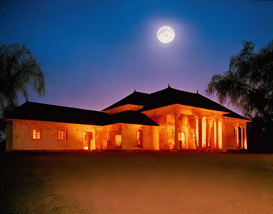 Colonial-style building at night with full moon, clear sky, and trees