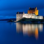 Majestic castle with towers reflected in lake under dusky sky