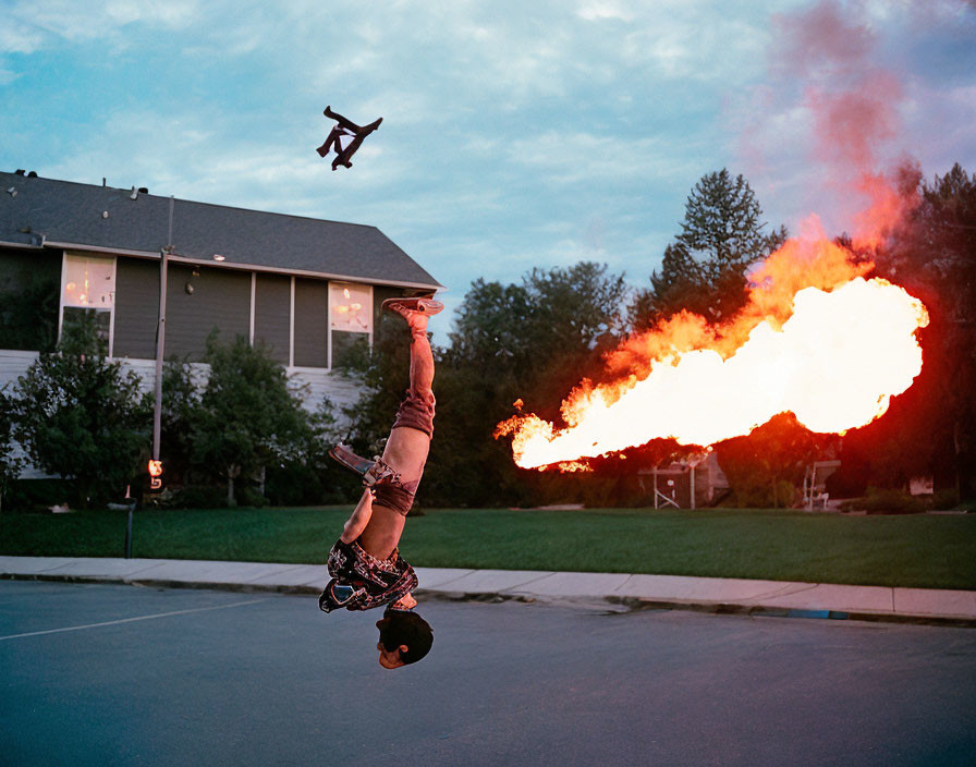 Person breathing fire in handstand on suburban street with drone and houses.