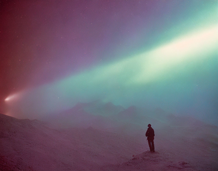 Solitary figure in snowy terrain under vibrant aurora borealis sky