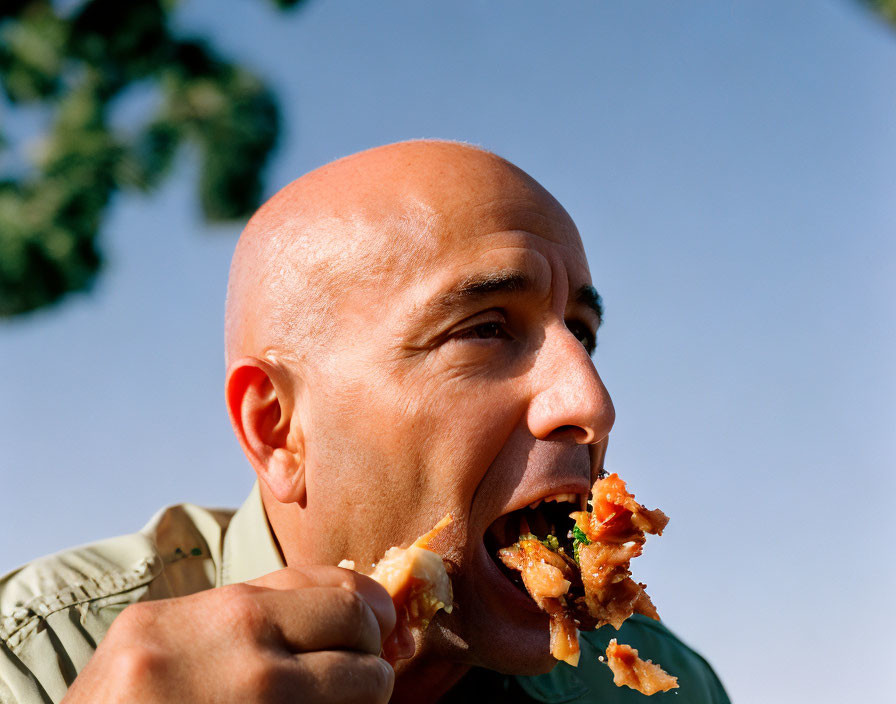 Bald Man Eating Large Food Outdoors Under Blue Sky