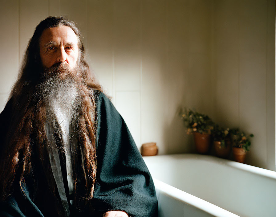 Bearded man in cloak by bathtub with plants in soft light