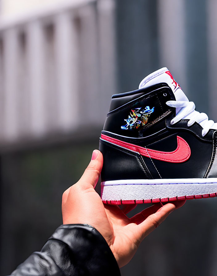 Black sneaker with red and white accents held in hand against urban backdrop