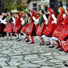 Women in traditional attire dancing by a pool with onlookers in folk costumes