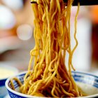 Colorful noodles and vegetables lifted by chopsticks in close-up shot