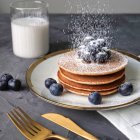 Pancakes with powdered sugar, berries, golden cutlery, and milk