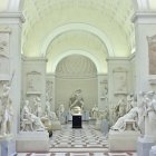 Luxurious art gallery with vaulted ceiling, marble floor, classical statues, and central walkway.